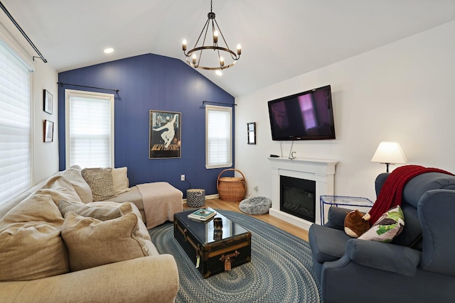 living room with a chandelier, wood finished floors, vaulted ceiling, healthy amount of natural light, and a glass covered fireplace