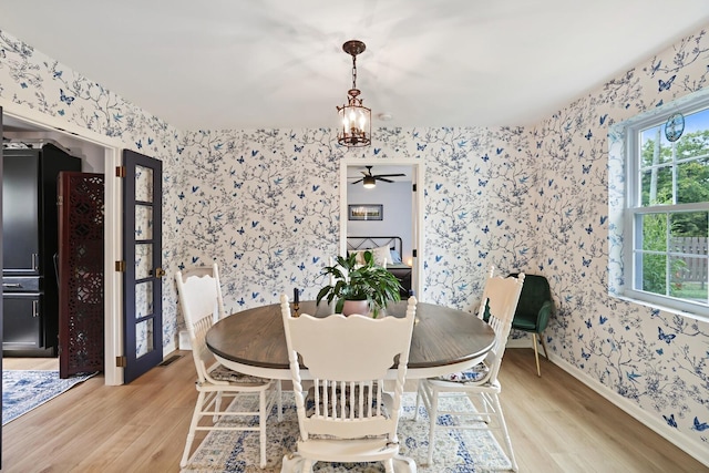 dining space featuring wallpapered walls, wood finished floors, a chandelier, baseboards, and a ceiling fan