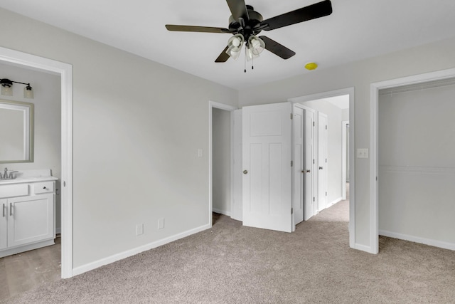 unfurnished bedroom with light colored carpet, baseboards, ensuite bathroom, a sink, and ceiling fan