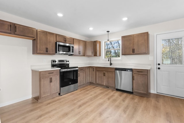 kitchen with appliances with stainless steel finishes, a sink, light wood-type flooring, light countertops, and recessed lighting
