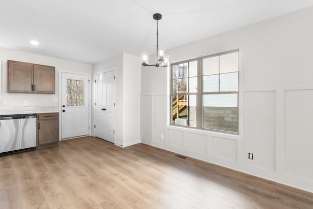 unfurnished dining area with a decorative wall, a chandelier, light wood-type flooring, healthy amount of natural light, and a wainscoted wall