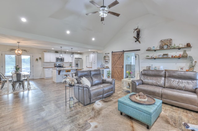 living area with a barn door, ceiling fan, recessed lighting, high vaulted ceiling, and light wood-style flooring