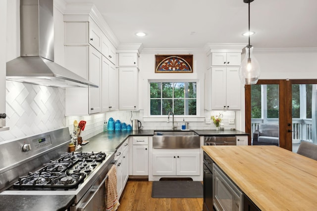 kitchen with appliances with stainless steel finishes, wall chimney exhaust hood, a sink, wooden counters, and white cabinetry
