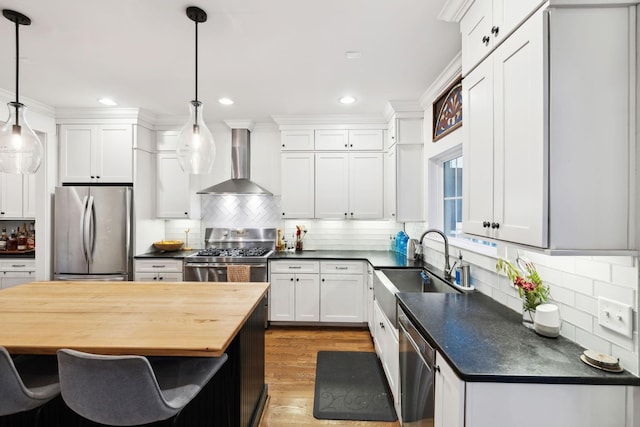 kitchen with stainless steel appliances, wall chimney exhaust hood, a sink, decorative backsplash, and recessed lighting