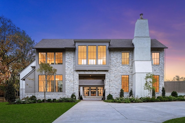 view of front facade with stone siding, a chimney, a front yard, and a shingled roof