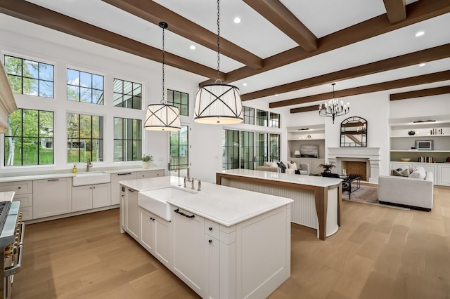 kitchen with a center island, beam ceiling, a sink, light wood-type flooring, and white cabinets