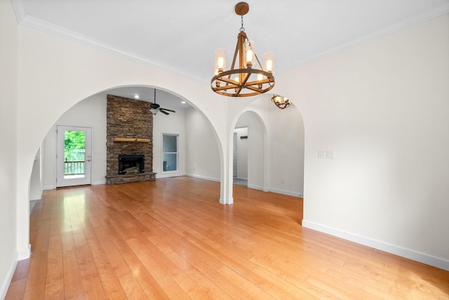 unfurnished living room with a ceiling fan, a chandelier, light wood-type flooring, a stone fireplace, and crown molding