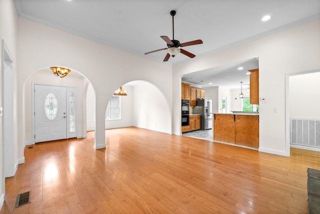 unfurnished living room featuring arched walkways, a chandelier, light wood finished floors, ceiling fan, and crown molding