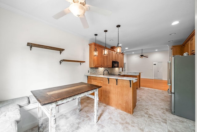 kitchen featuring freestanding refrigerator, a ceiling fan, a peninsula, black microwave, and a breakfast bar