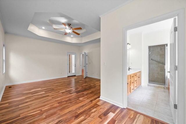 unfurnished room with a ceiling fan, light wood finished floors, baseboards, and a tray ceiling