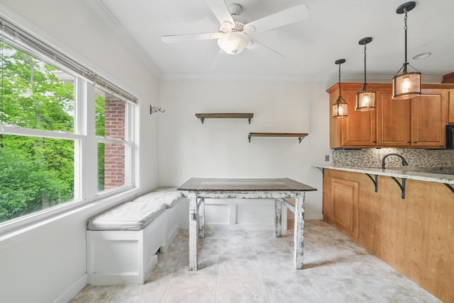 kitchen featuring brown cabinets, ceiling fan, baseboards, decorative backsplash, and crown molding
