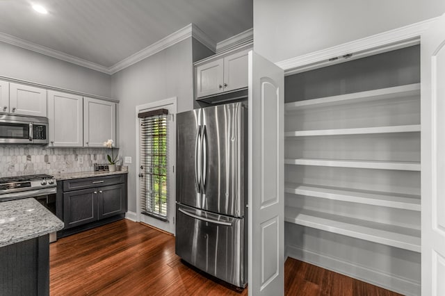 kitchen with appliances with stainless steel finishes, light stone countertops, tasteful backsplash, ornamental molding, and dark wood-style floors