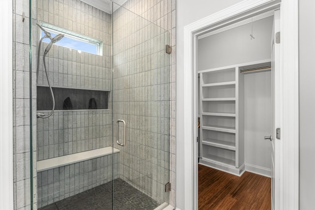 bathroom with wood finished floors, a shower stall, a spacious closet, baseboards, and ornamental molding