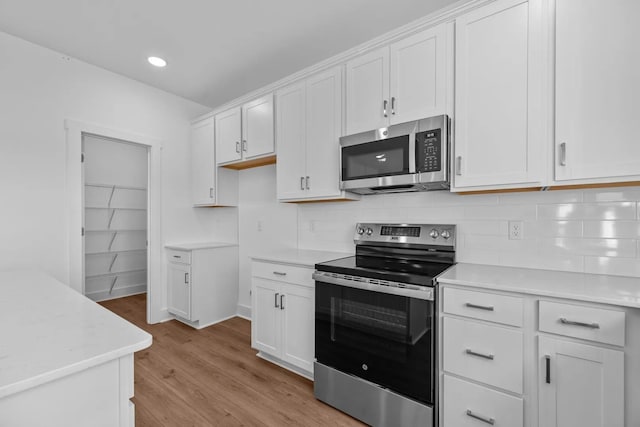 kitchen with stainless steel appliances, light countertops, white cabinetry, light wood-style flooring, and decorative backsplash
