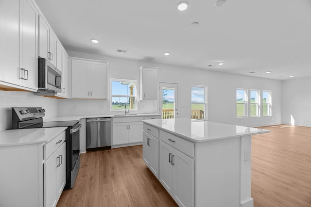 kitchen featuring appliances with stainless steel finishes, light wood-type flooring, decorative backsplash, white cabinetry, and a center island