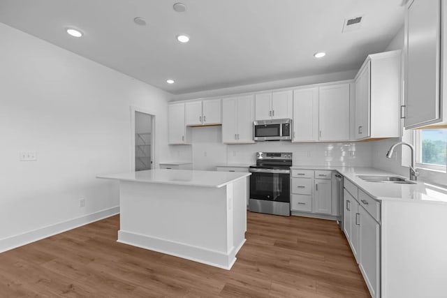 kitchen with appliances with stainless steel finishes, a sink, wood finished floors, light countertops, and recessed lighting