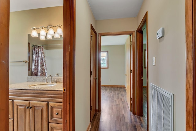 hall with a sink, wood finished floors, and baseboards