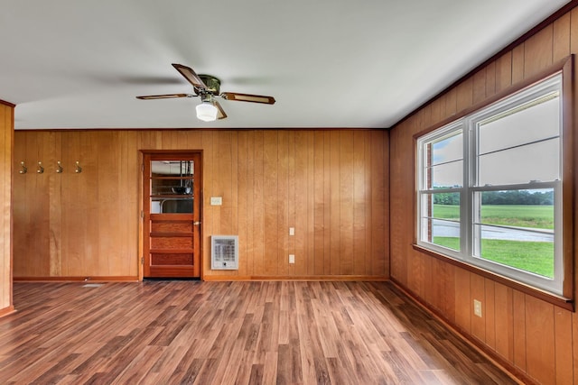unfurnished room with heating unit, wood finished floors, baseboards, a ceiling fan, and wood walls