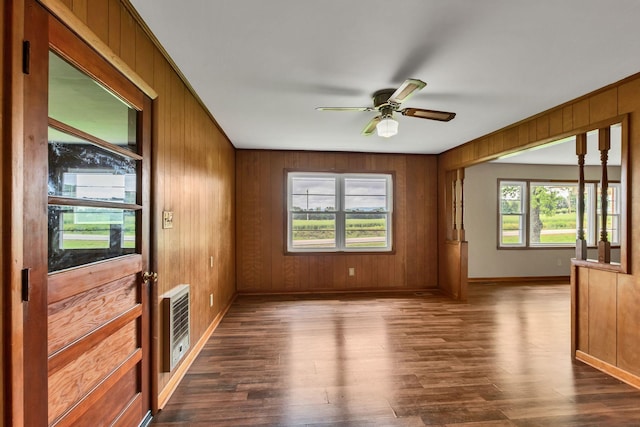spare room with dark wood finished floors, baseboards, heating unit, wooden walls, and a ceiling fan