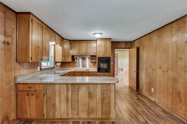 kitchen with black appliances, a sink, light countertops, brown cabinets, and wood finished floors