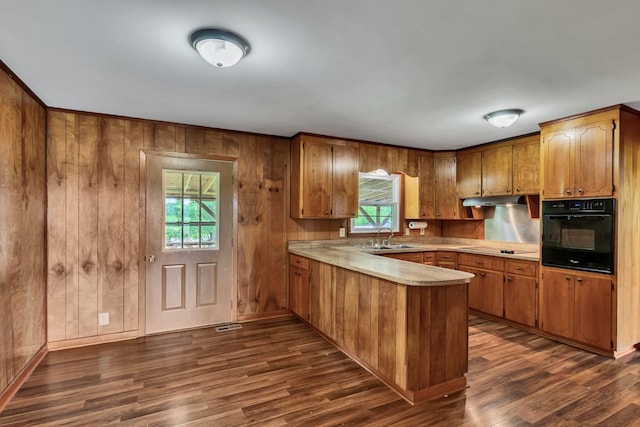 kitchen with black appliances, a peninsula, brown cabinetry, light countertops, and wood walls