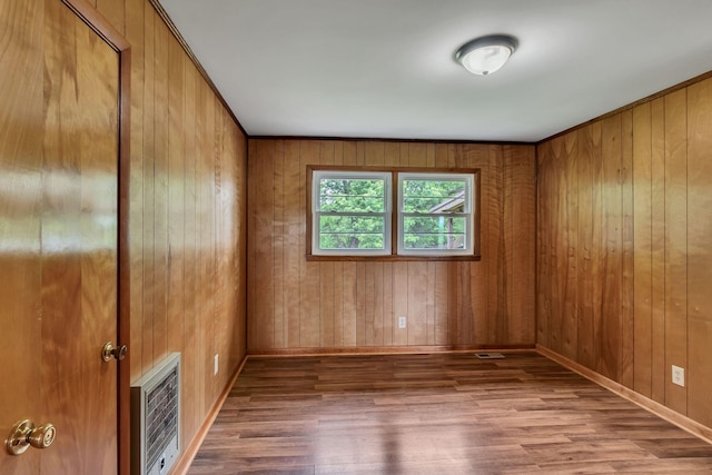 spare room with heating unit, wood finished floors, wood walls, and baseboards