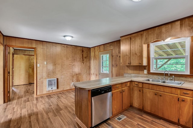 kitchen with dishwasher, a sink, light countertops, light wood-style flooring, and wood walls