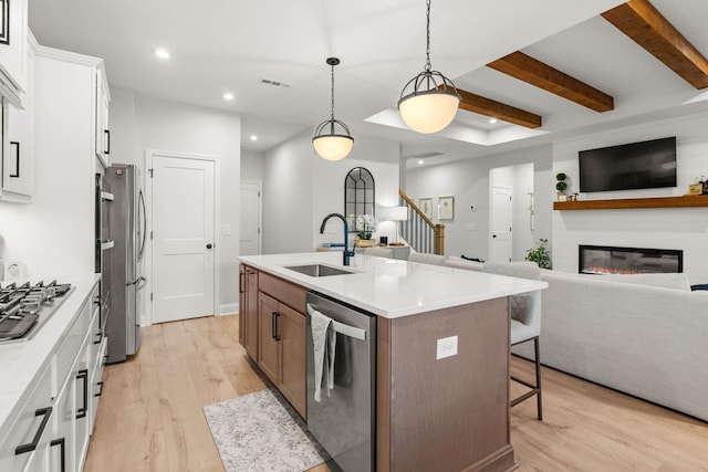 kitchen featuring stainless steel appliances, a sink, open floor plan, light wood-style flooring, and recessed lighting