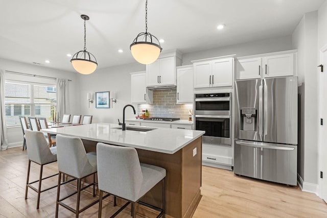 kitchen featuring appliances with stainless steel finishes, a sink, light wood-type flooring, recessed lighting, and backsplash