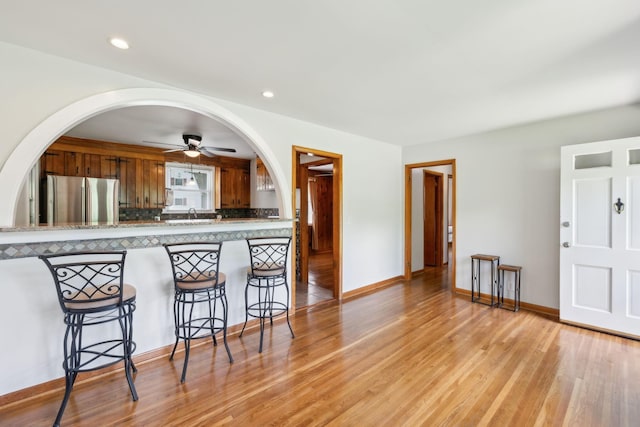 kitchen featuring freestanding refrigerator, brown cabinets, a kitchen breakfast bar, ceiling fan, and light wood-style floors