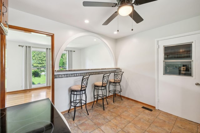 kitchen featuring a breakfast bar, baseboards, a ceiling fan, recessed lighting, and stone finish floors