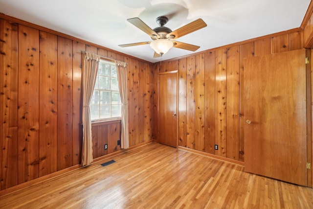 spare room with light wood-type flooring, baseboards, ceiling fan, and wood walls