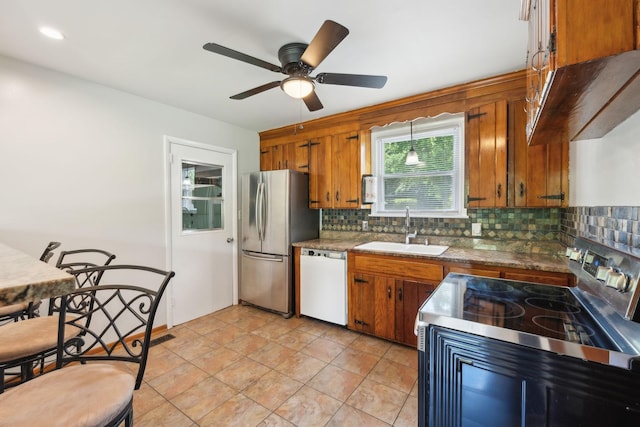 kitchen with stainless steel appliances, a sink, brown cabinetry, and backsplash
