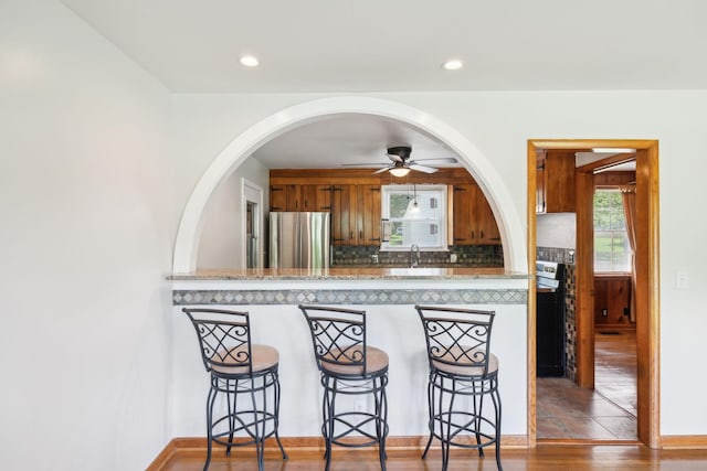 kitchen with appliances with stainless steel finishes, brown cabinets, backsplash, ceiling fan, and a sink
