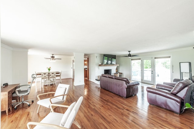 living area with a ceiling fan, a brick fireplace, and wood finished floors