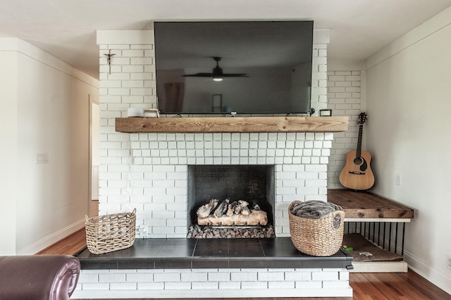 detailed view of a brick fireplace, wood finished floors, baseboards, and a ceiling fan