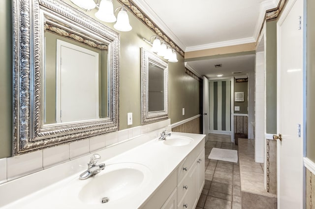 full bath with crown molding, double vanity, wallpapered walls, and a wainscoted wall