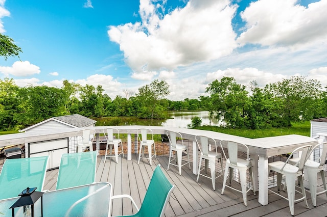 wooden terrace with a water view, outdoor dining space, and view of wooded area