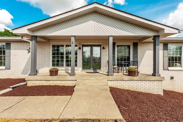doorway to property with covered porch, brick siding, and french doors
