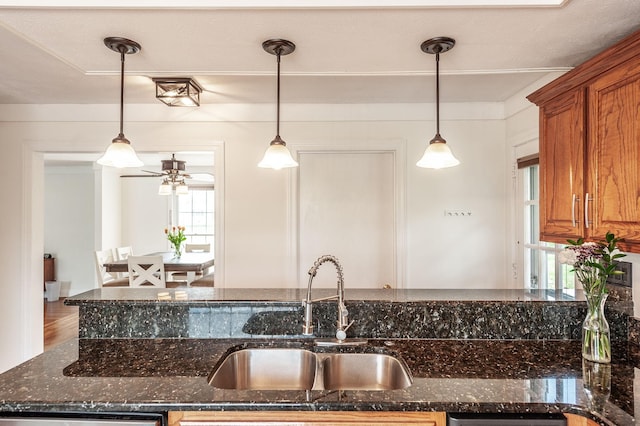 kitchen with a sink, brown cabinetry, decorative light fixtures, and dark stone counters