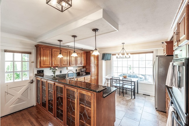 kitchen featuring brown cabinets, freestanding refrigerator, dark stone countertops, and pendant lighting