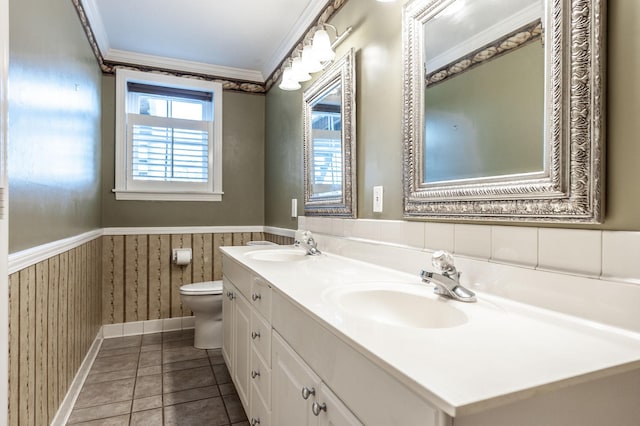 bathroom with crown molding, a wainscoted wall, toilet, double vanity, and baseboards