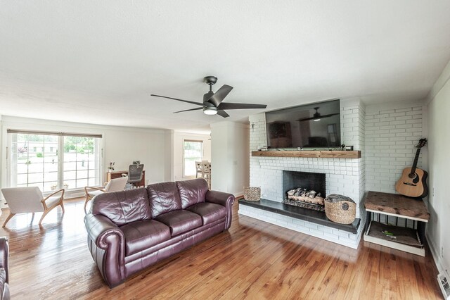 living room featuring ceiling fan, light wood finished floors, and a brick fireplace