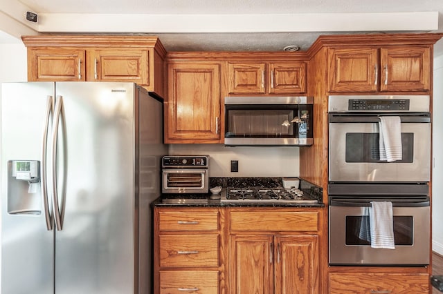 kitchen featuring appliances with stainless steel finishes, brown cabinetry, and dark stone countertops