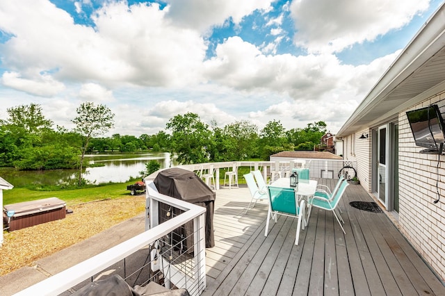 wooden deck with a water view, outdoor dining space, a hot tub, and view of wooded area