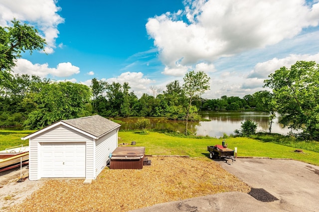 view of green lawn with a water view, an outbuilding, a hot tub, a garage, and view of wooded area