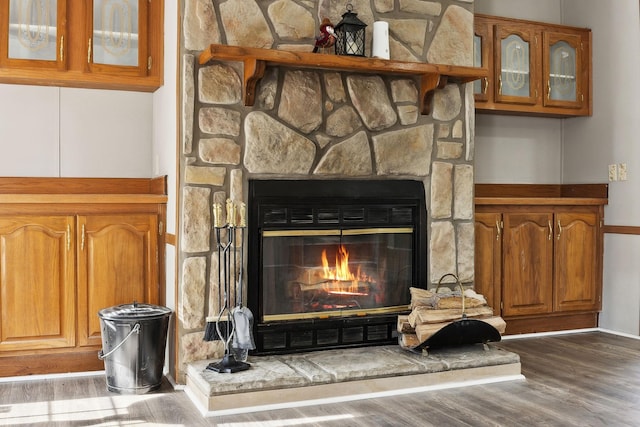 detailed view of wood finished floors, a stone fireplace, and baseboards