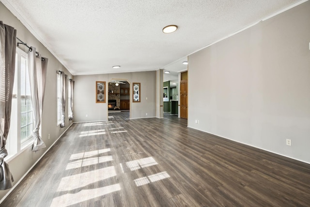 unfurnished living room featuring wood finished floors, a textured ceiling, healthy amount of natural light, crown molding, and baseboards