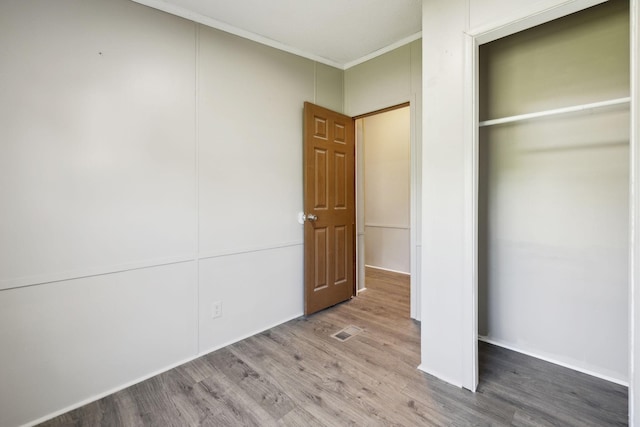 unfurnished bedroom with ornamental molding, wood finished floors, and a closet