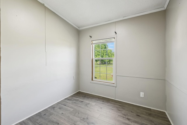 empty room with wood finished floors, ornamental molding, and baseboards